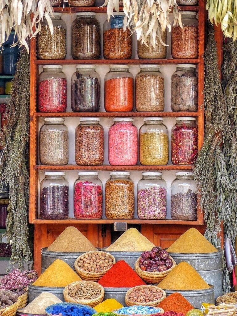 Display of Moroccan spices and herbs in jars and conical piles outside a traditional apothecary shop in a medina.