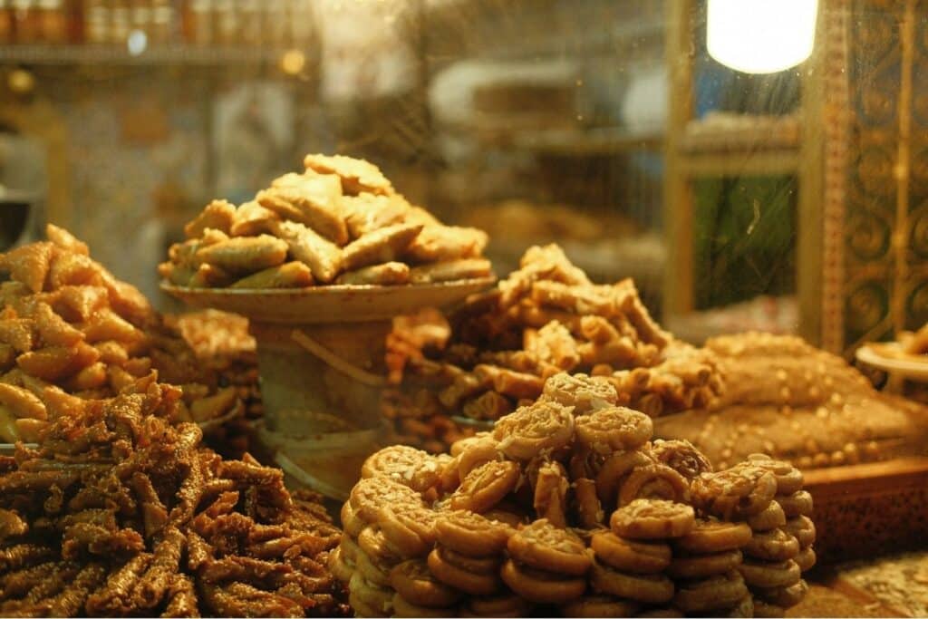 A variety of traditional Moroccan pastries stacked on trays in a bakery, including chebakia, briouats, and almond-filled sweets.