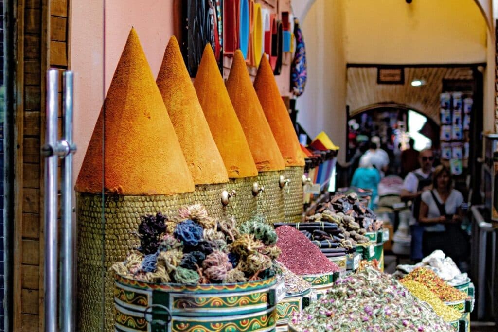 Traditional Moroccan spices shop with colorful cones of turmeric and baskets filled with herbs, flowers, and dried roots in a lively souk.